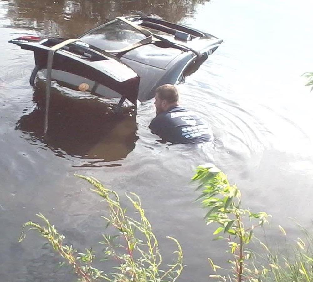 An Aces Towing crew member chest-deep in the bayou, securing straps to a sunken car